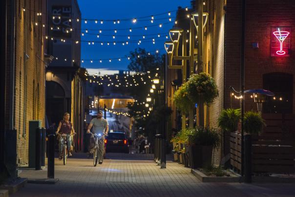 A couple rides bikes in downtown underneath the alley lights